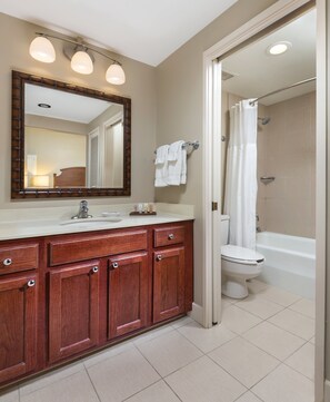 A bathroom with a wooden vanity, a large mirror, a shower with a curtain, and a toilet.