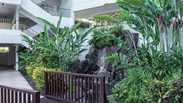Ein mehrgeschossiges Atrium mit einer zentralen Wasserspiels, umgeben von üppiger Vegetation und einer Holzterrasse.