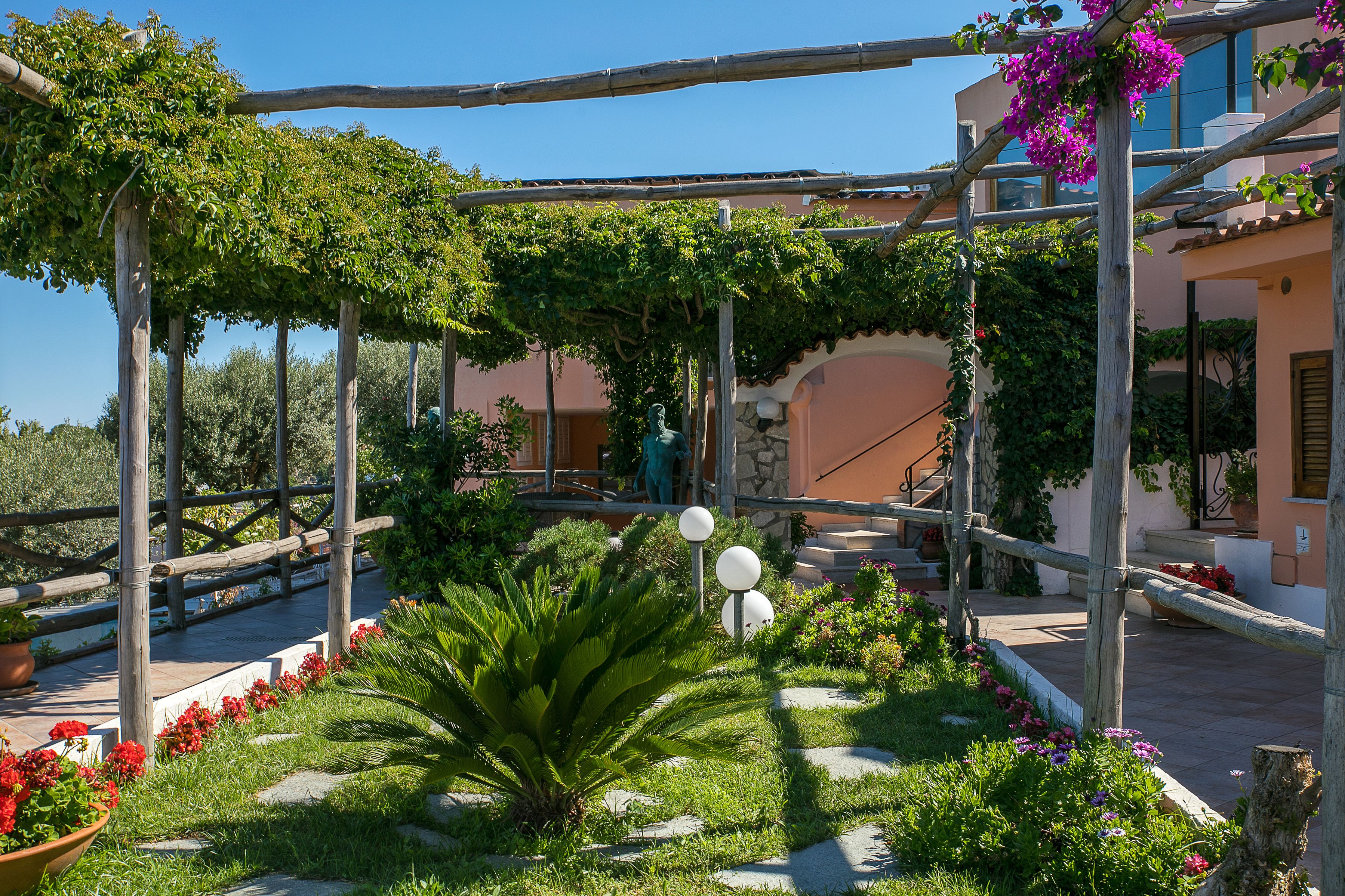 A garden with a pergola, potted plants, and a statue.
