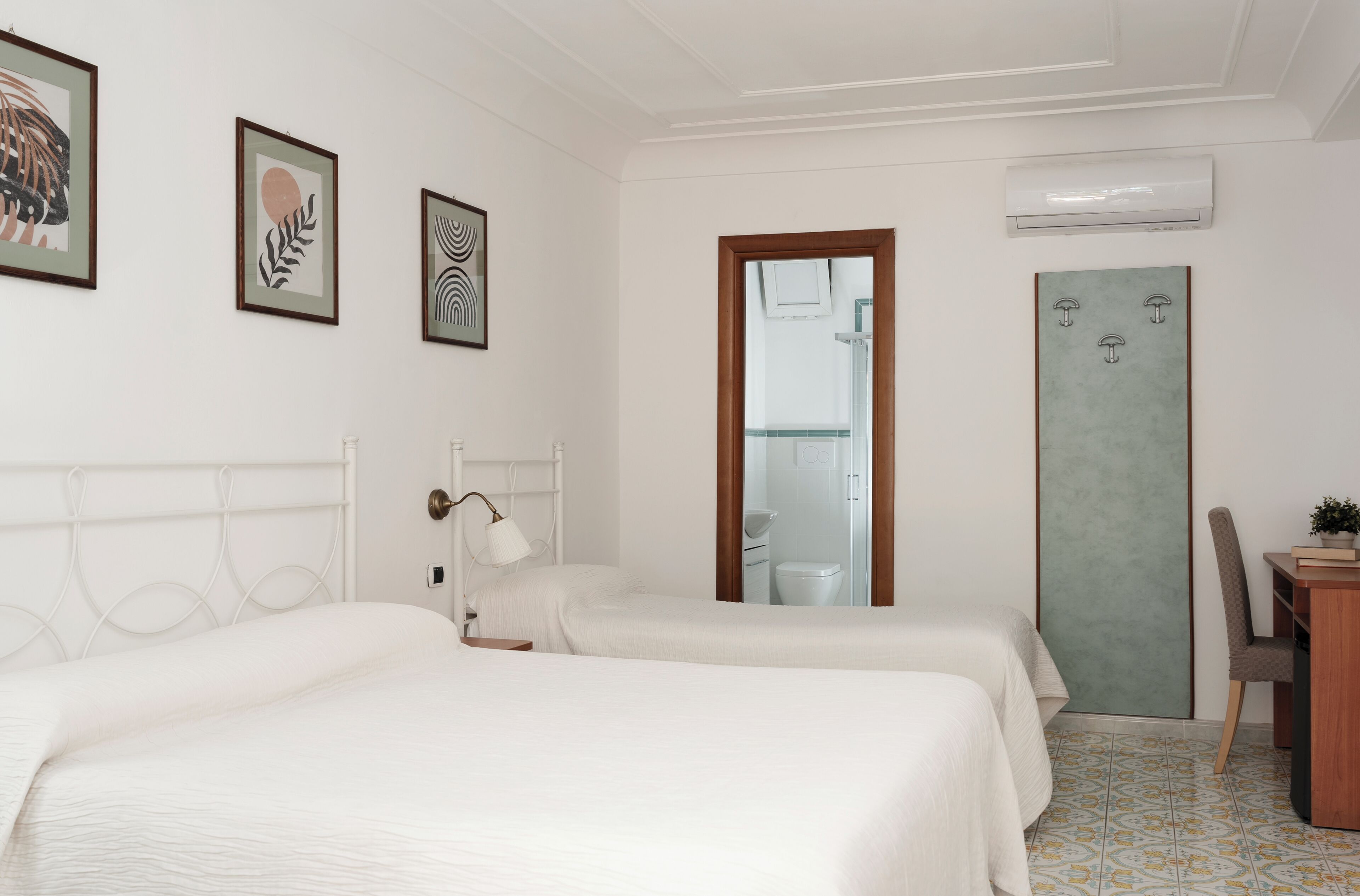 A hotel room with two beds, a desk, a chair, a mirror, and framed artwork on the wall.