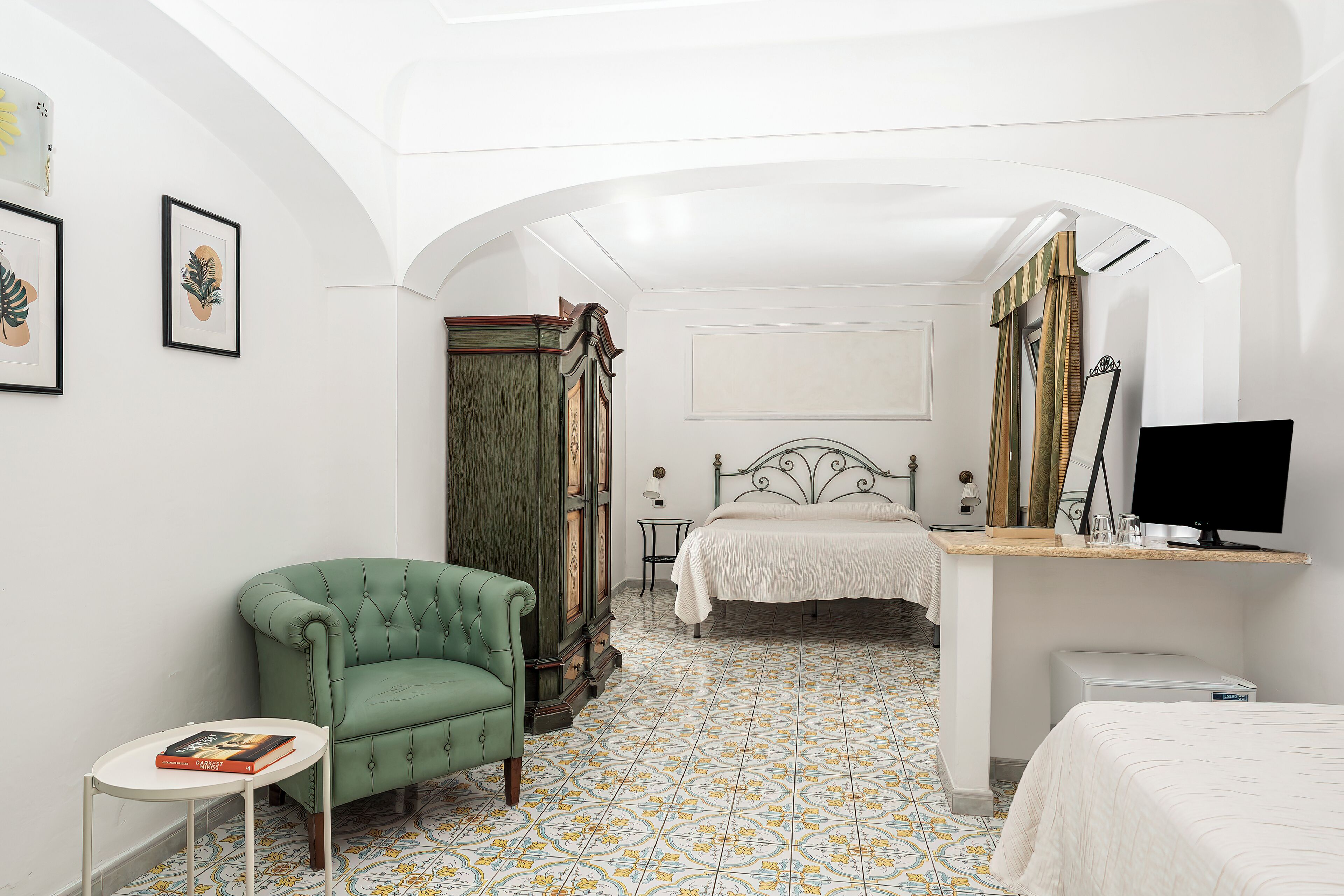 A bedroom with a green armchair, a bed, a desk, and a television.
