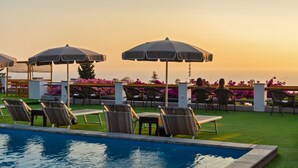A poolside area with lounge chairs and umbrellas, a pool, and a view of the ocean at sunset. - Hotel Il Girasole (Anacapri)