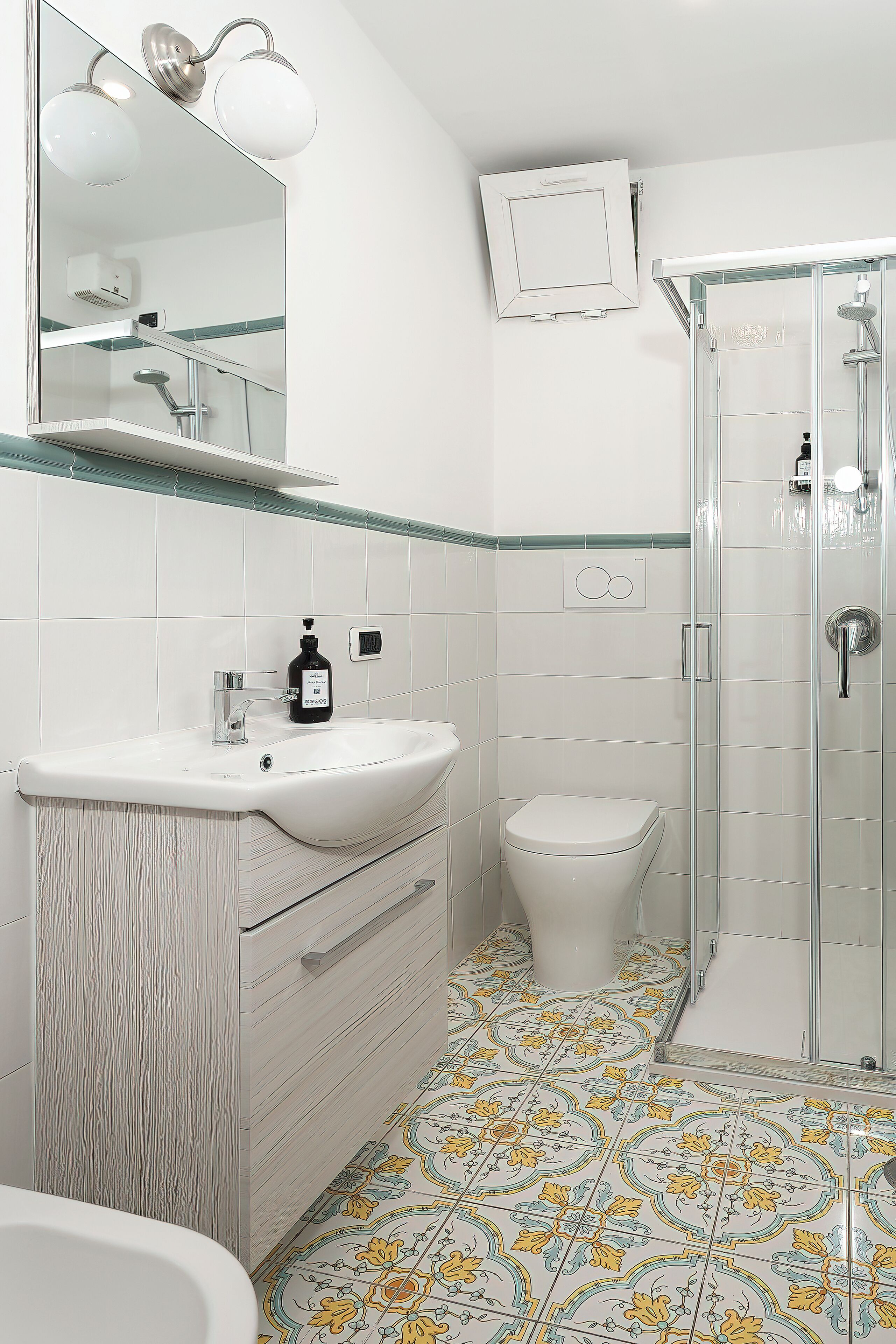 A bathroom with a white sink, a toilet, a shower enclosure, and a mirror with lights.