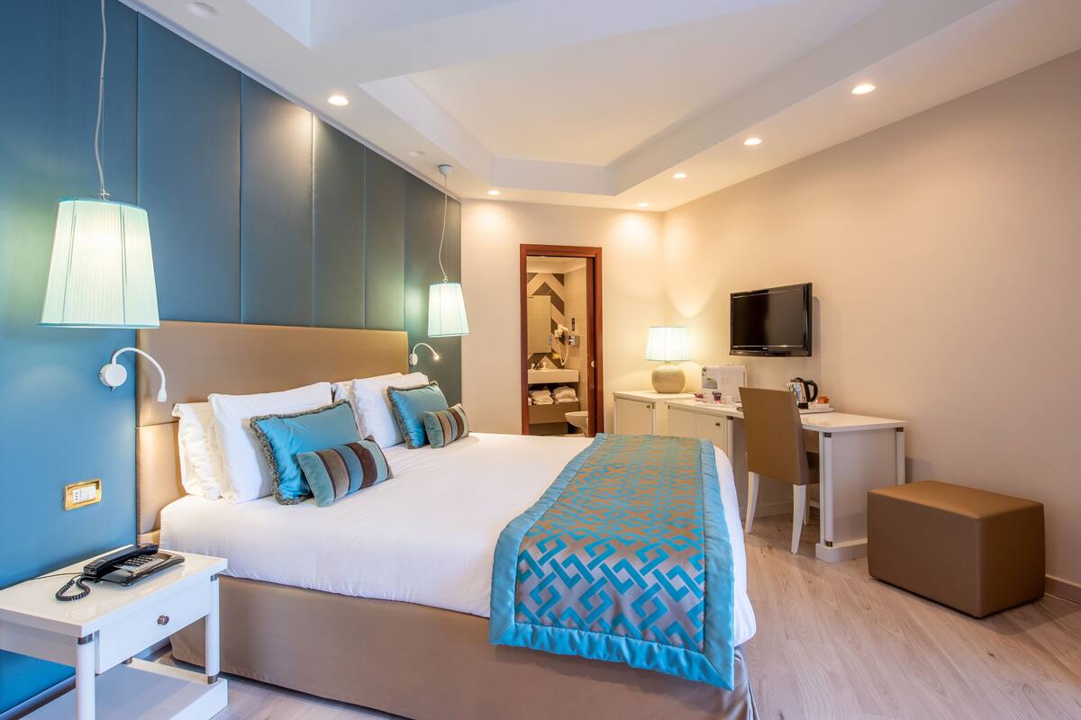 A modern hotel room with a large bed, bedside tables, a desk, a television, and a wardrobe.