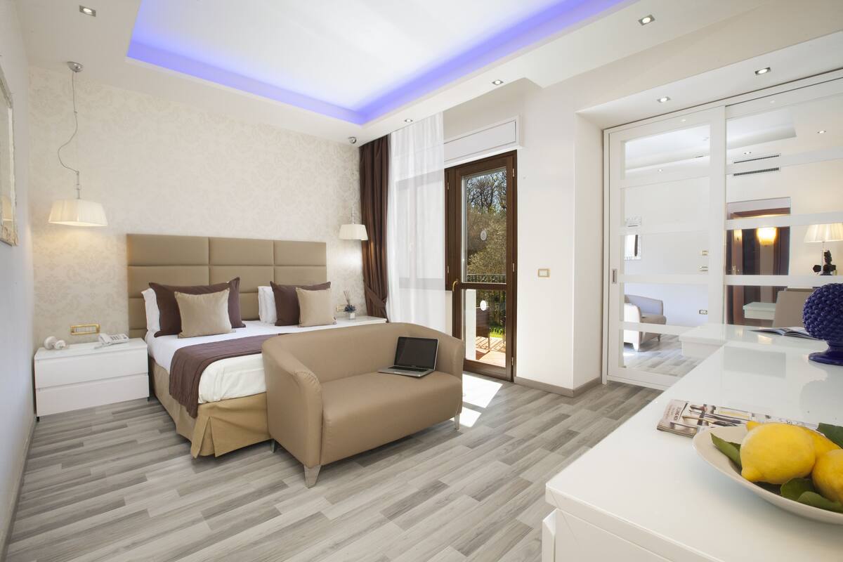 A modern bedroom with a bed, a sofa, a laptop, and a dining area with a table and chairs.