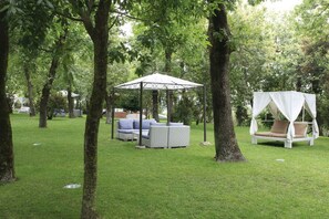 Un porxo, una cadira bressol i un conjunt de sofàs en una zona exterior enjardinada i envoltada d'arbres.