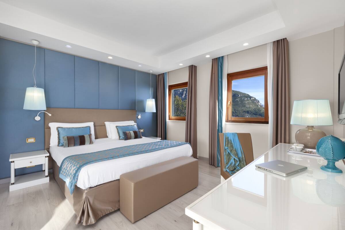 A modern hotel room with a large bed, bedside tables, a desk, and a view of the outdoors.