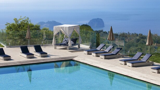 A poolside area with lounge chairs and a canopy, overlooking a body of water and greenery.