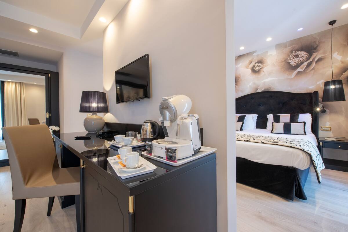 A modern hotel room with a desk, coffee maker, and a bed with a black headboard.