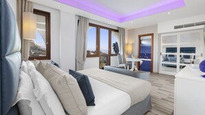 A modern hotel room with a large bed, a desk, and a view of the sea.