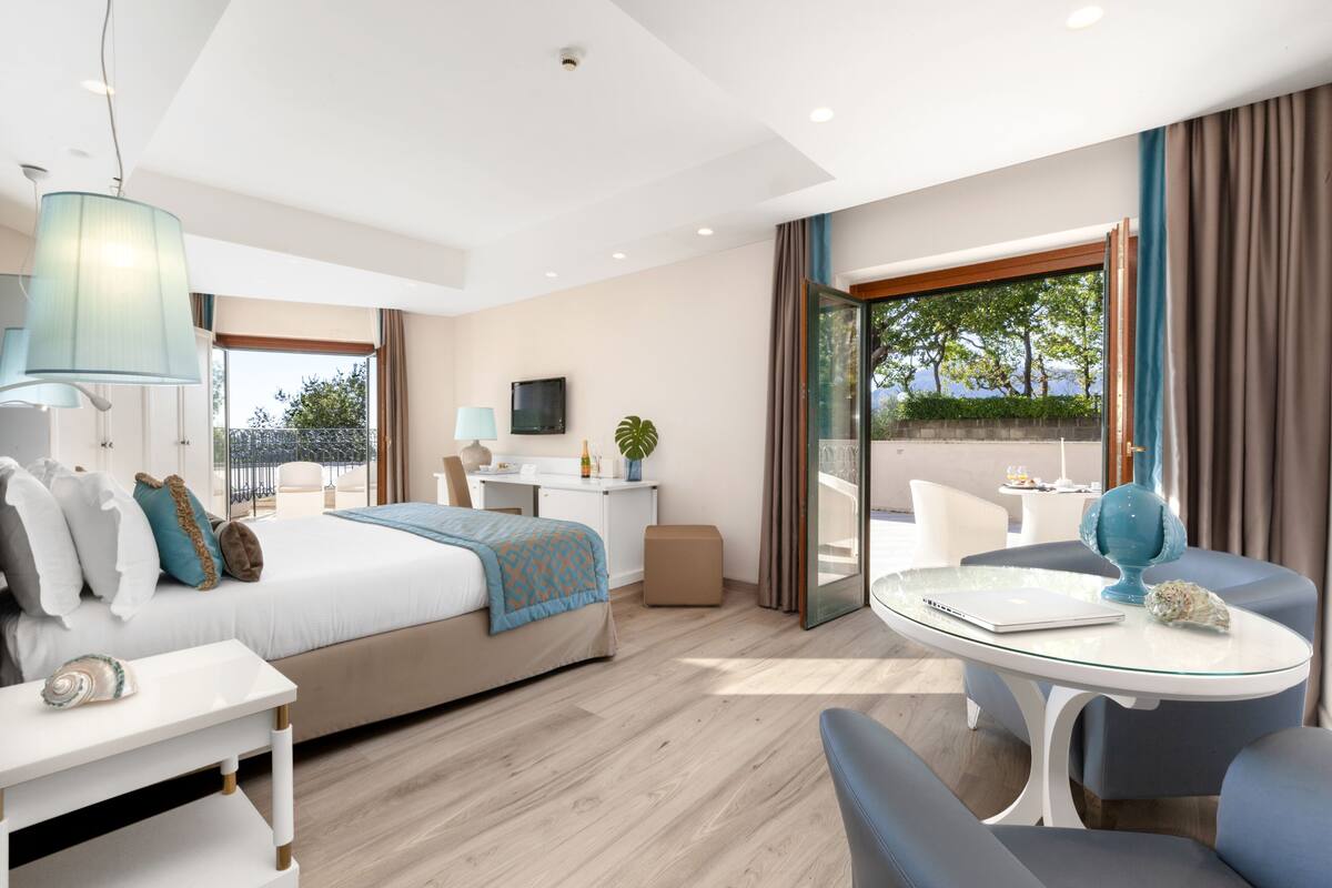 A modern hotel room with a bed, a desk, a laptop, a globe, and a balcony with a view.