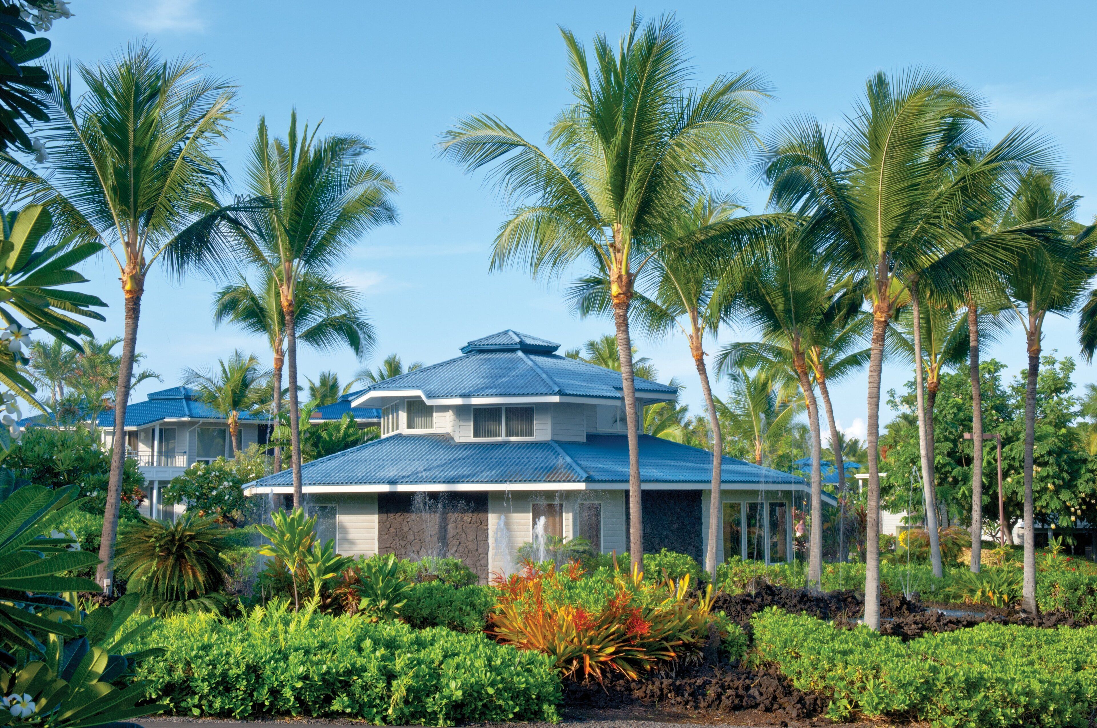 A resort with a two-story building, surrounded by lush tropical vegetation and palm trees.