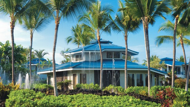 Un resort con un edificio de dos pisos, palmeras y un jardín bien cuidado.