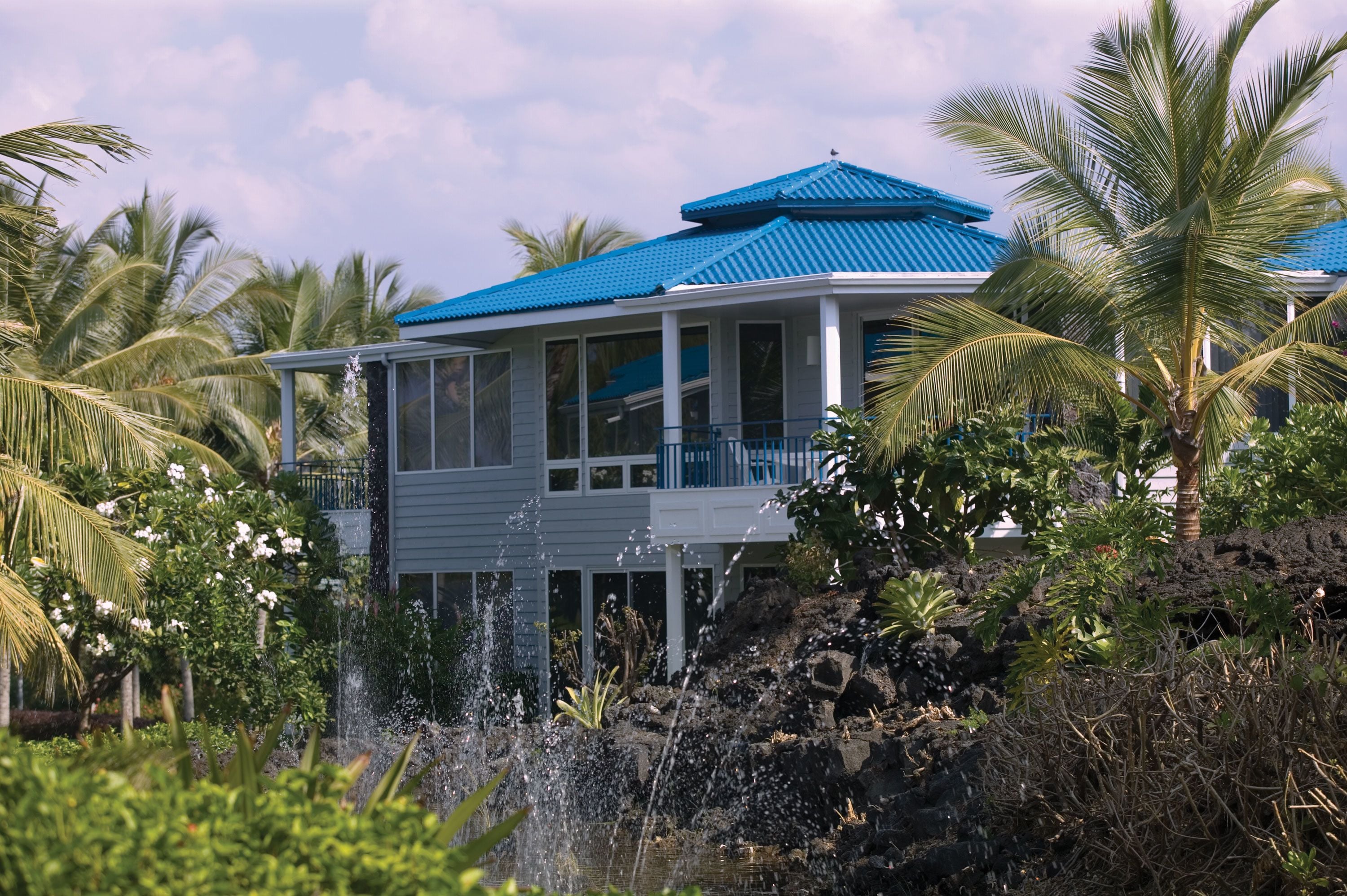 A house with a blue roof, surrounded by lush greenery and a small water feature.