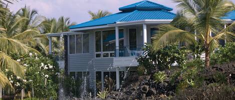 A house with a blue roof, surrounded by lush greenery and a small water feature.