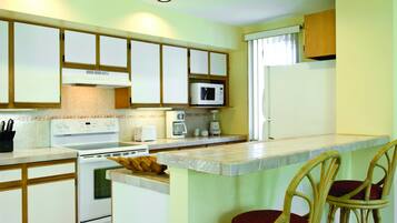 A kitchen with a stove, microwave, and coffee maker. There are chairs and a window.