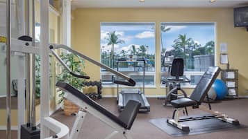 Una palestra con attrezzature per esercizi, ampie finestre e vista su palme.