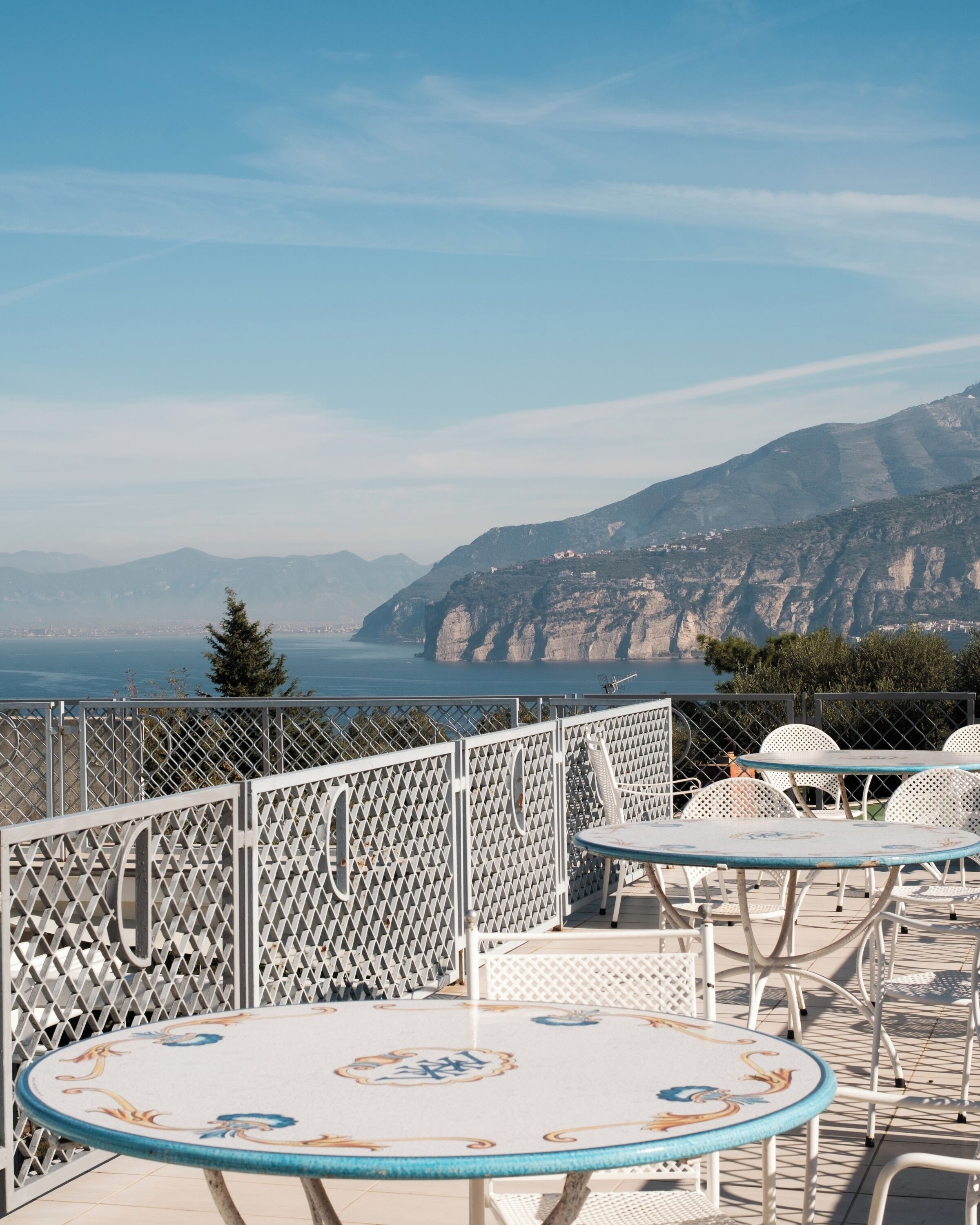 A terrace with outdoor seating, overlooking a mountainous coastline.