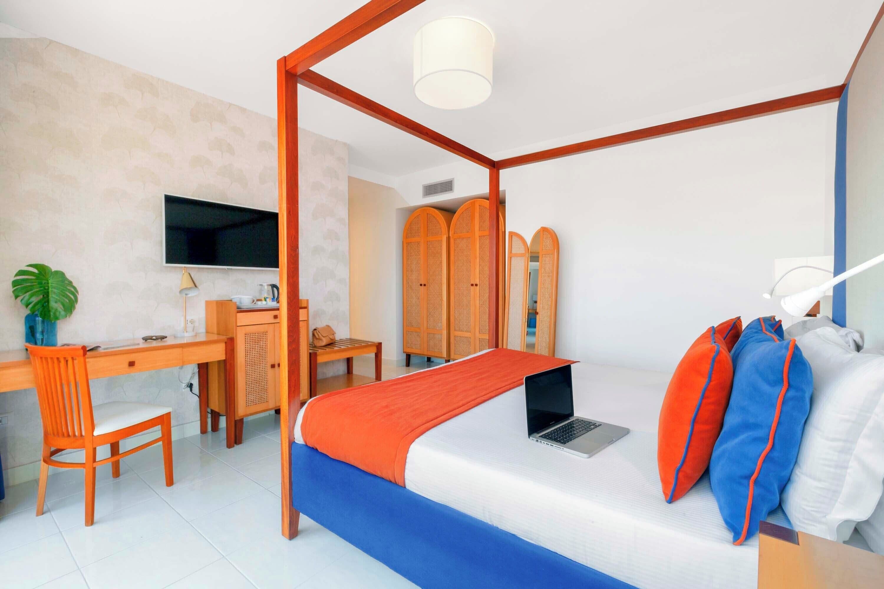 Un dormitorio con cama con dosel, un escritorio con silla, un televisor y un guardarropa.