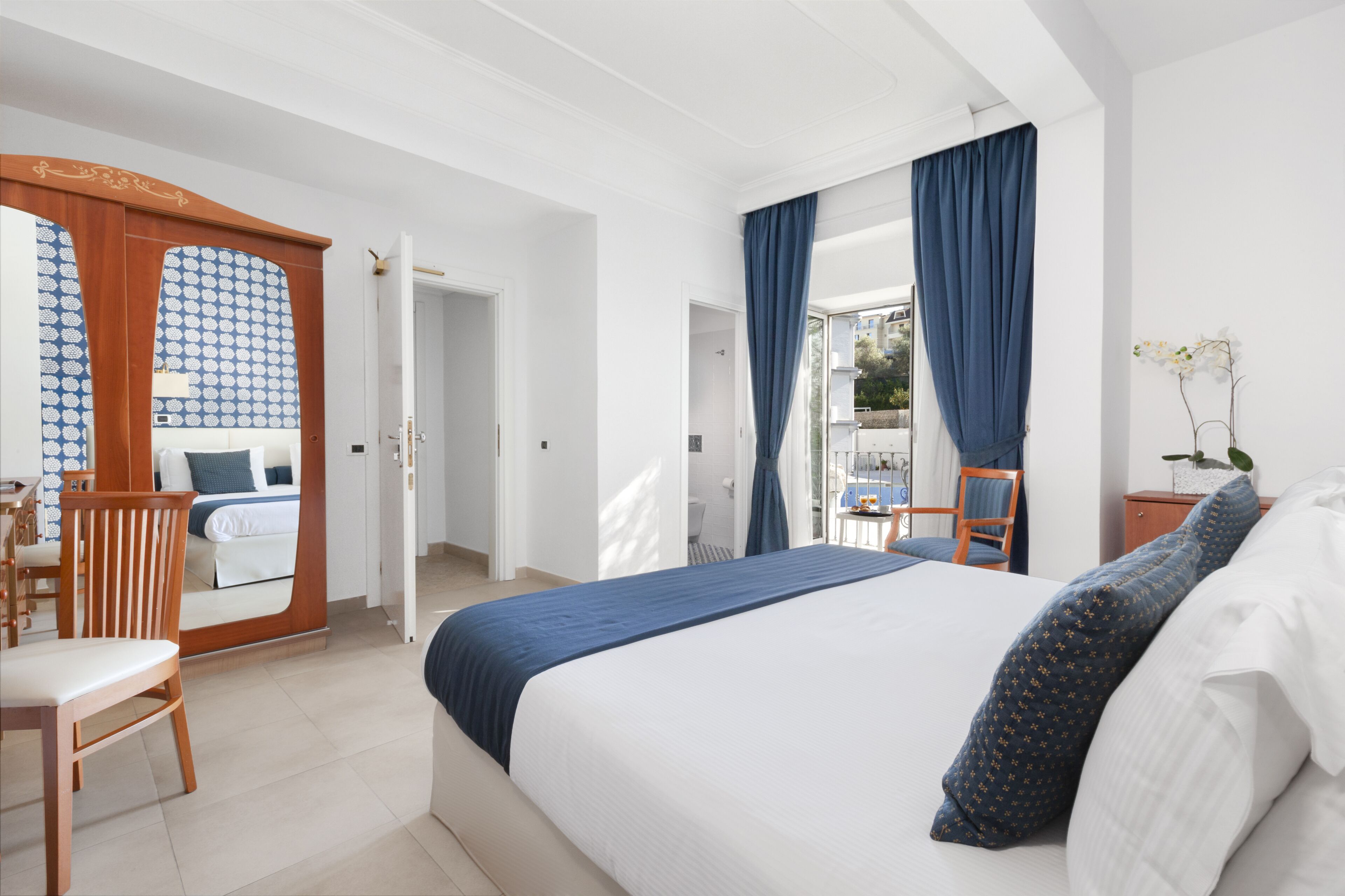 Ein Hotelzimmer mit einem Bett, einem Holzstuhl, einem Schreibtisch und Blick ins Freie.