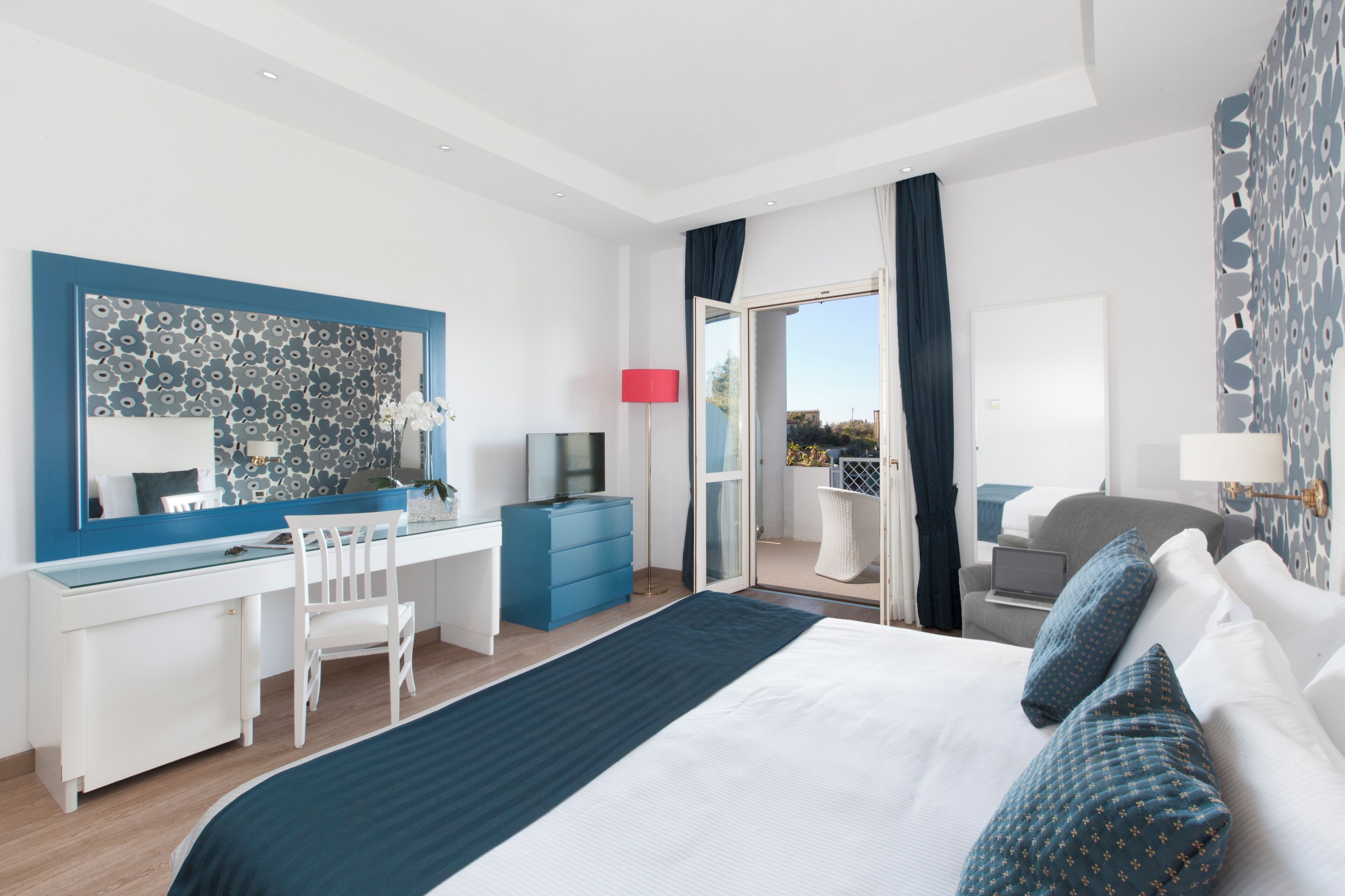 Ett modernt hotellrum med en stor säng, ett skrivbord med en stol, en TV och en balkong med utsikt.