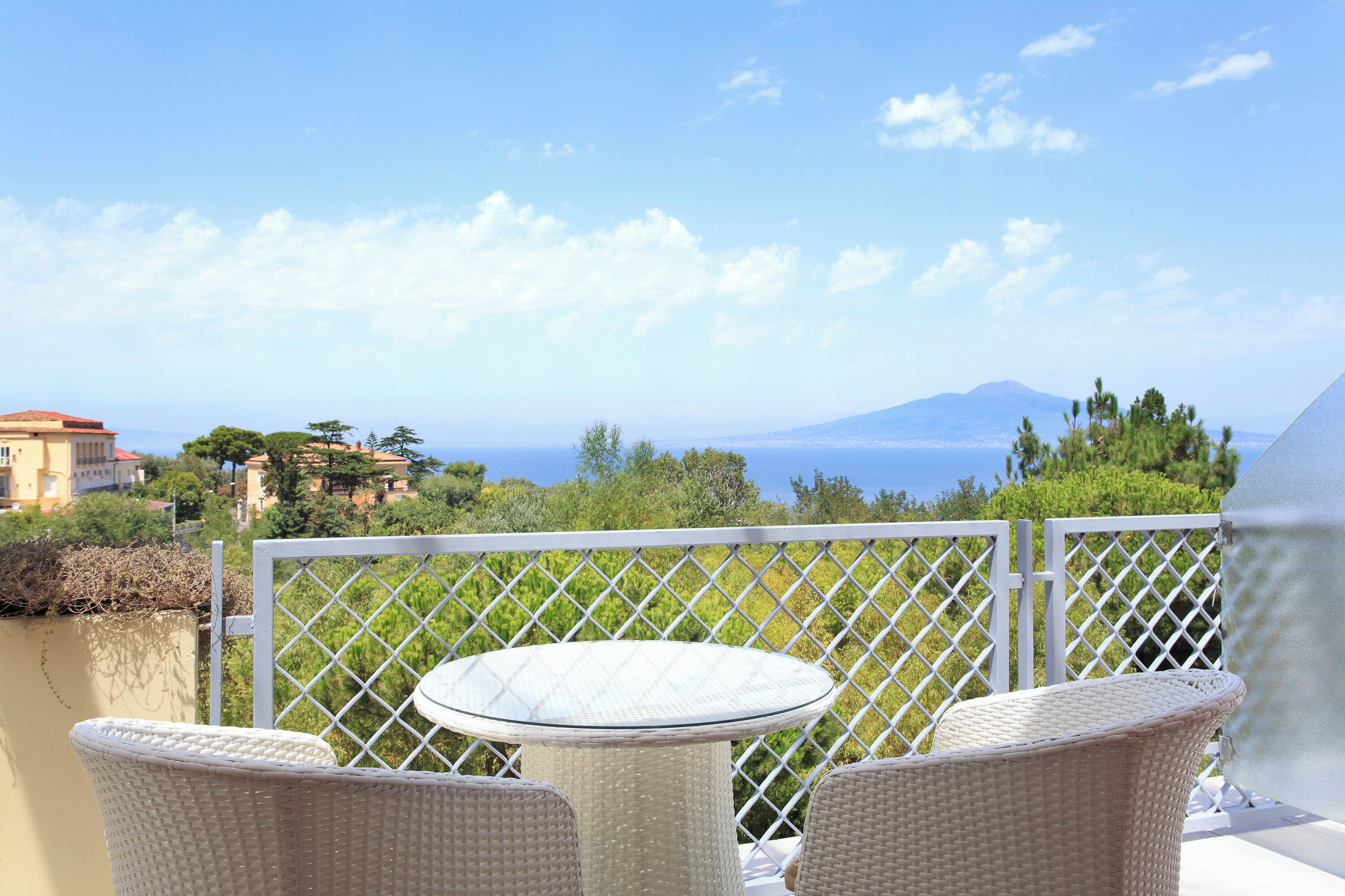 A balcony with wicker furniture and a view of the sea and a mountain.