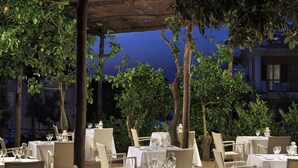 An outdoor dining area with tables set for two, surrounded by wicker chairs and covered by a wooden pergola. - Atlantic Palace Hotel (Sorrento)