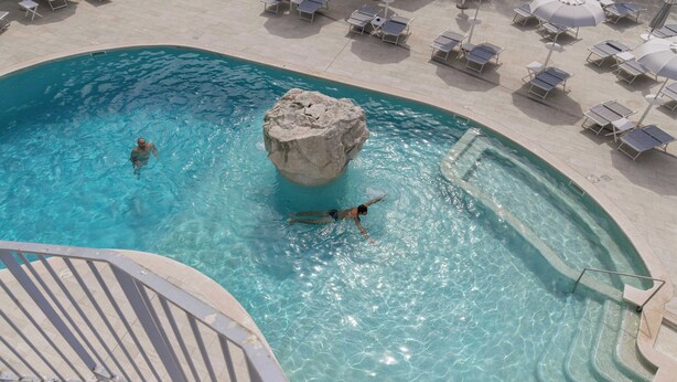 A pool with a rock feature, lounge chairs, and a poolside area. - Atlantic Palace Hotel (Sorrento)