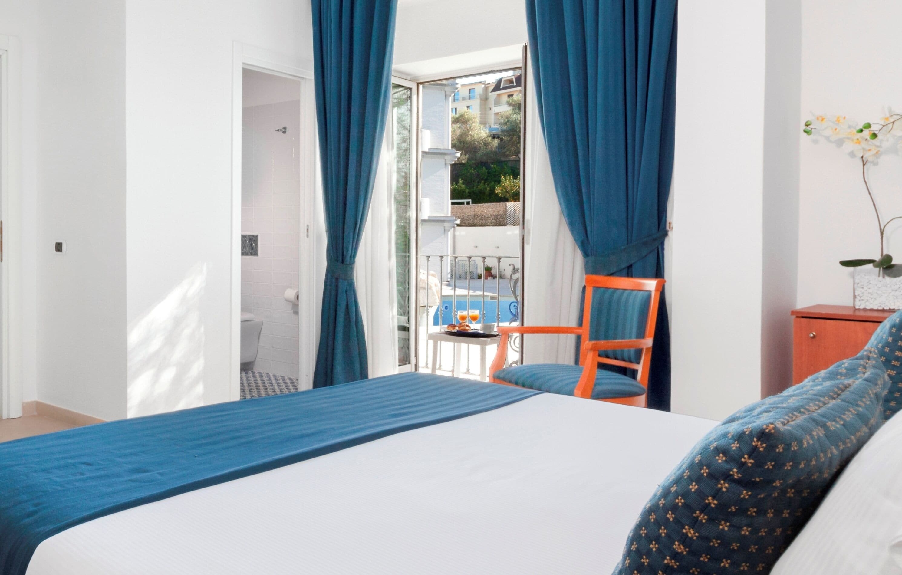 Ein Schlafzimmer mit Bett, Sessel, einem kleinen Tisch mit einem Getränk und einem Balkon mit Geländer.