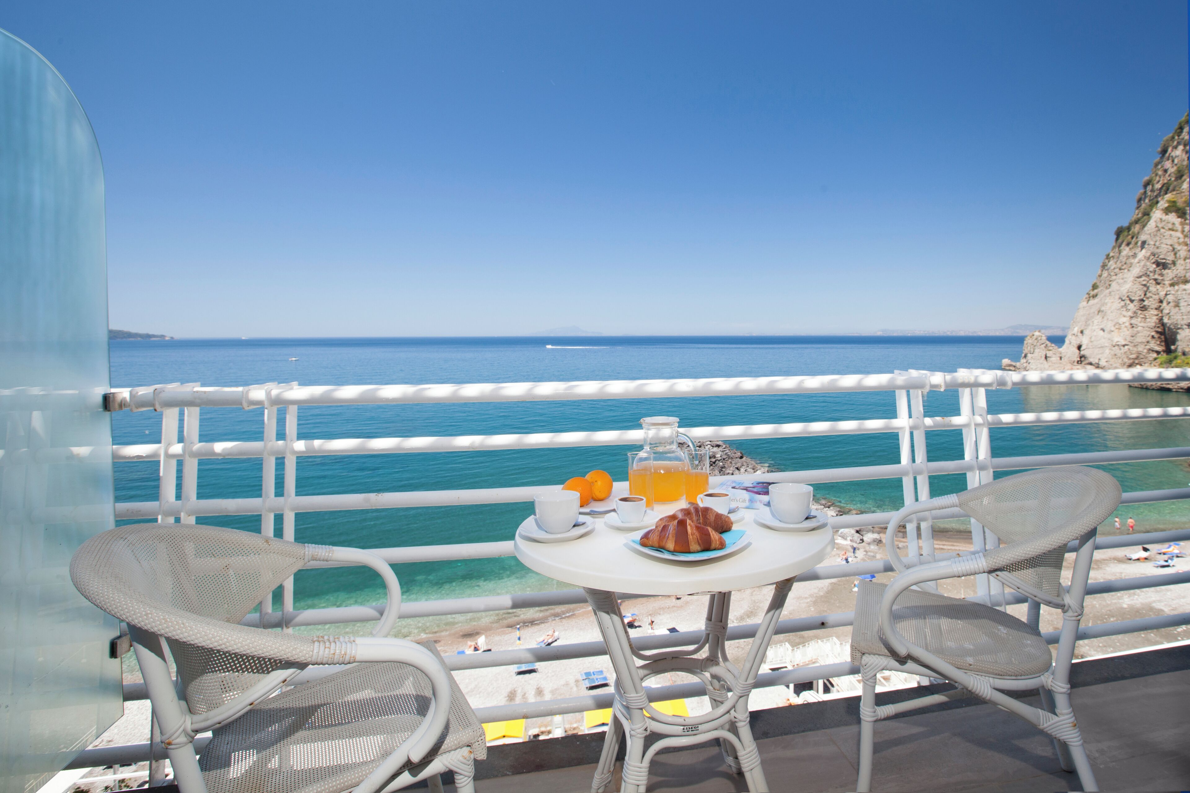 A balcony with a table set for breakfast overlooking a beach.