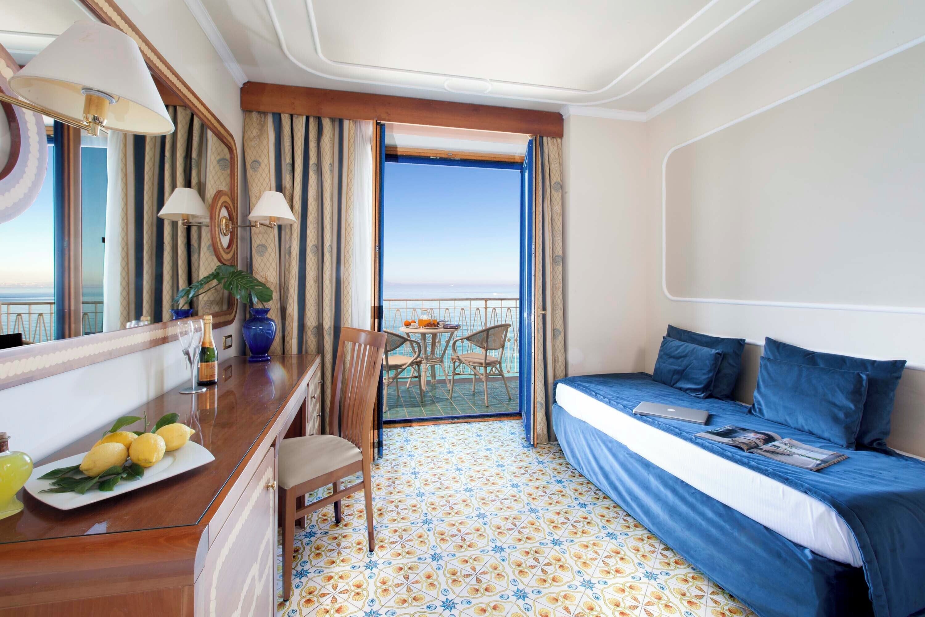 Une chambre d’hôtel avec un lit, un bureau avec un ordinateur portable, une chaise, une petite table avec une plante et un balcon avec vue.