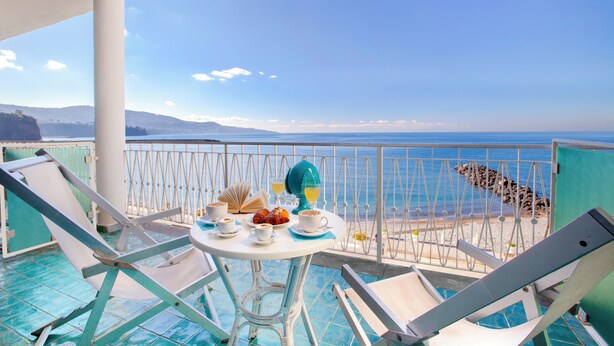 A balcony with a table set for breakfast, overlooking a beach and the sea.