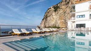 A pool area with sun loungers and a view of the sea.