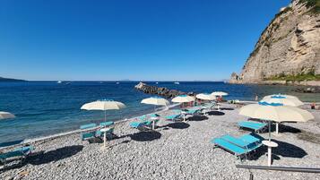 Privat strand, svart sandstrand, solstolar och parasoller