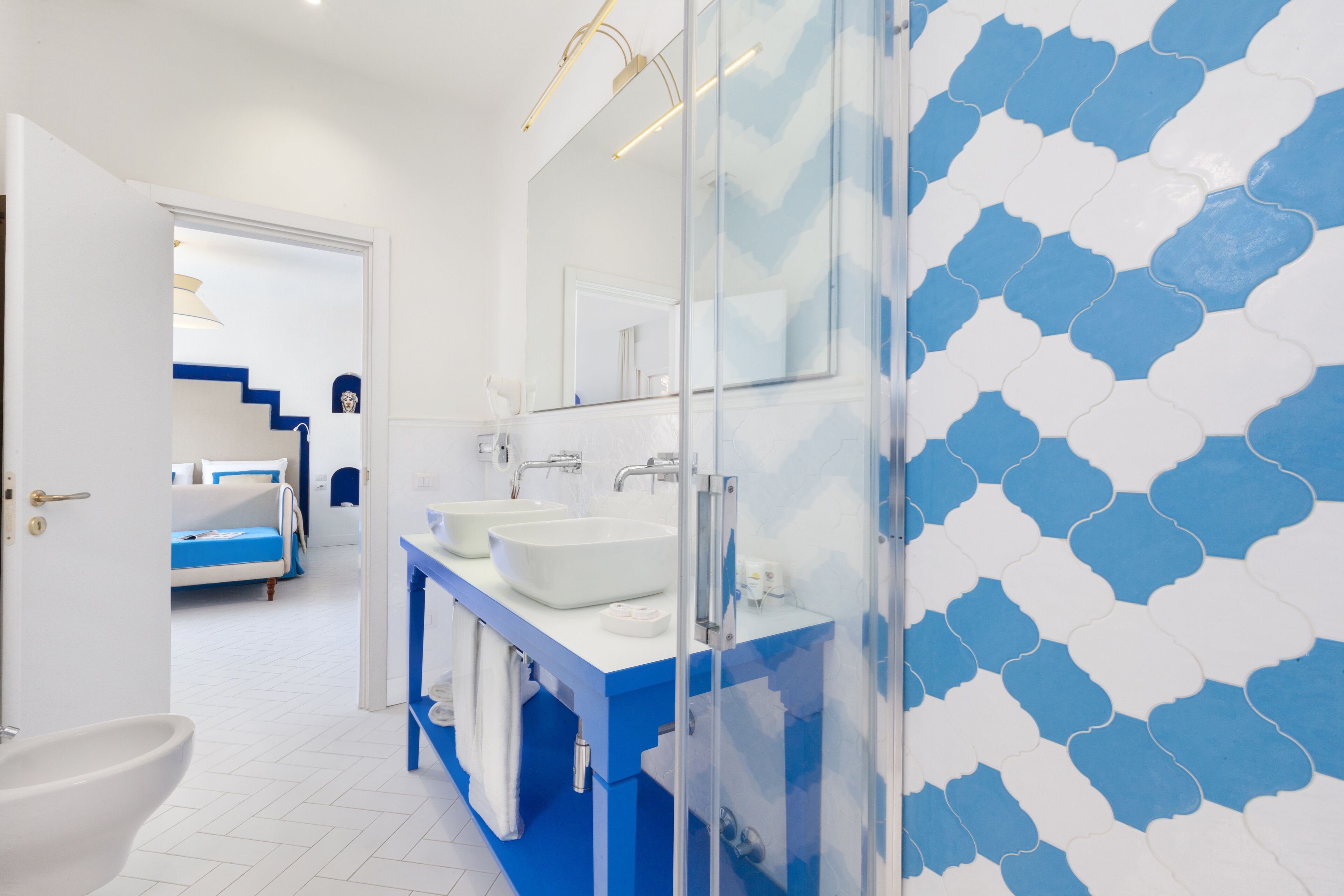 A modern bathroom with a blue and white tile backsplash, a glass shower enclosure, and a white sink vanity.