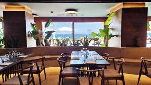 A restaurant with a view of the ocean, featuring tables set for dining, chairs, and large windows.