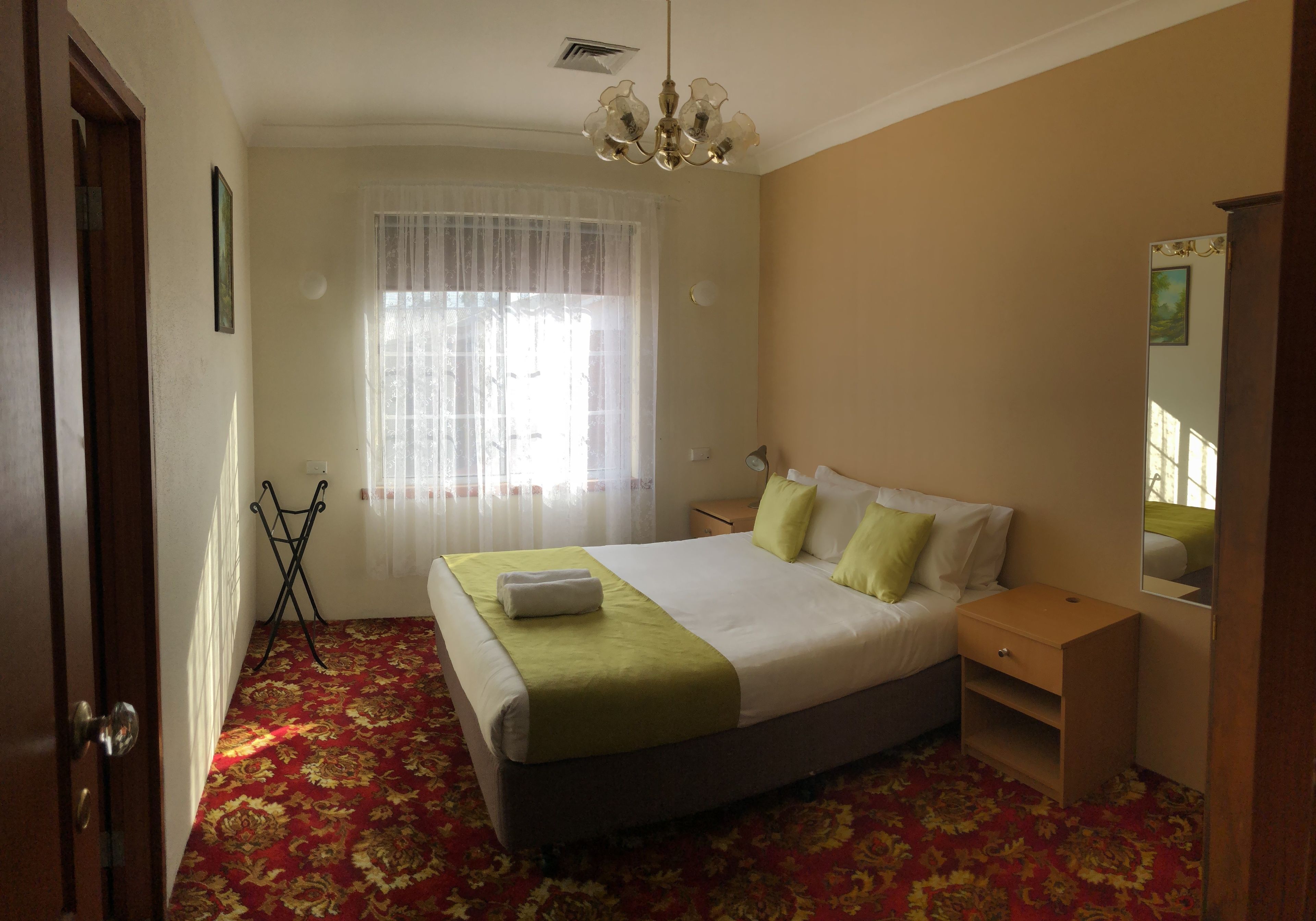 A hotel room with a bed, bedside table, nightstand, and a mirror.