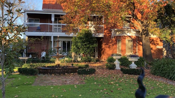 A two-story house with a brick facade, a balcony, and a well-maintained garden with a lawn and flower beds. - Meramie Motor Inn (Albury)