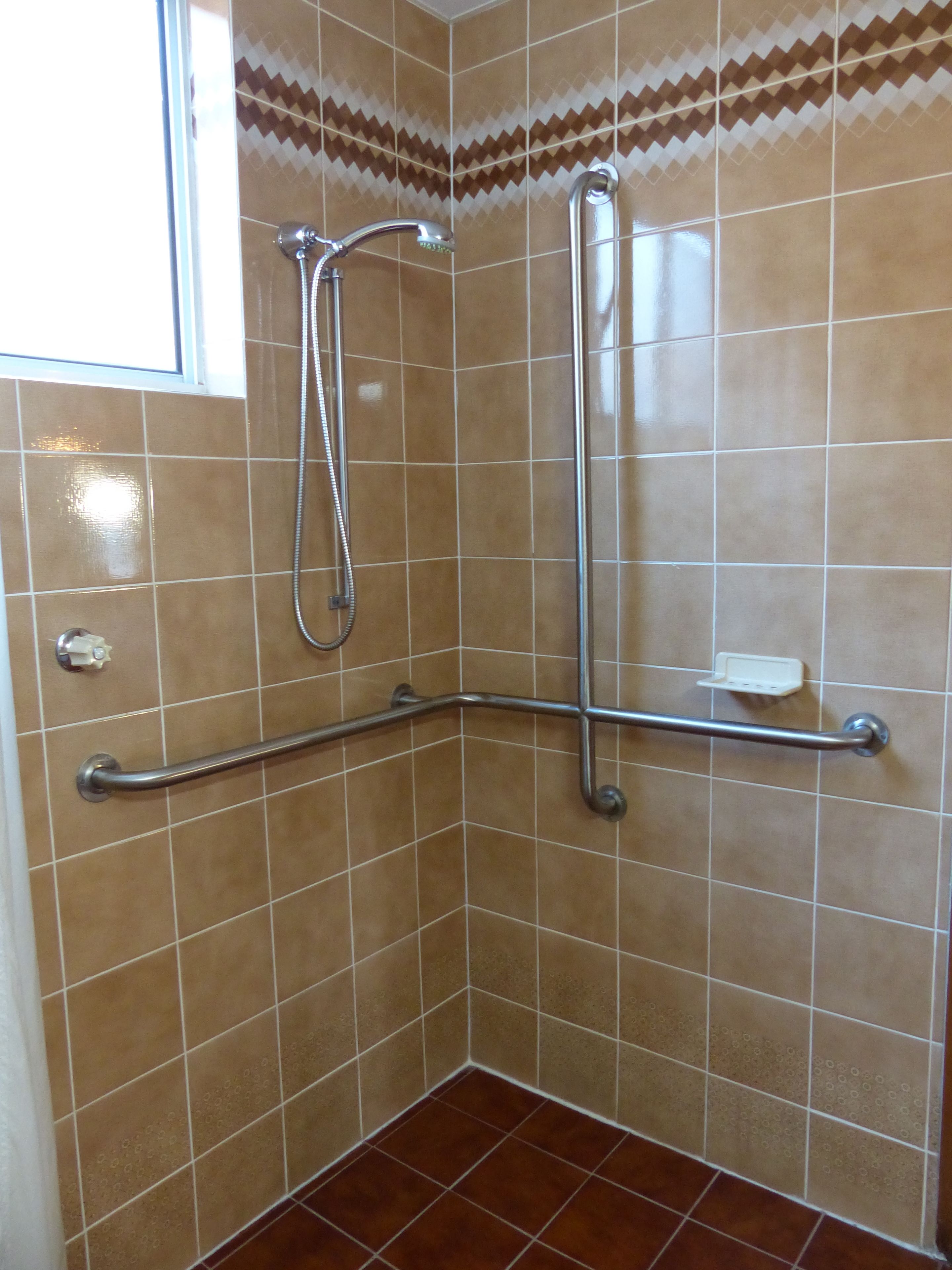 Ducha en esquina con barra de apoyo, cabezal de ducha de mano y grifo empotrado.