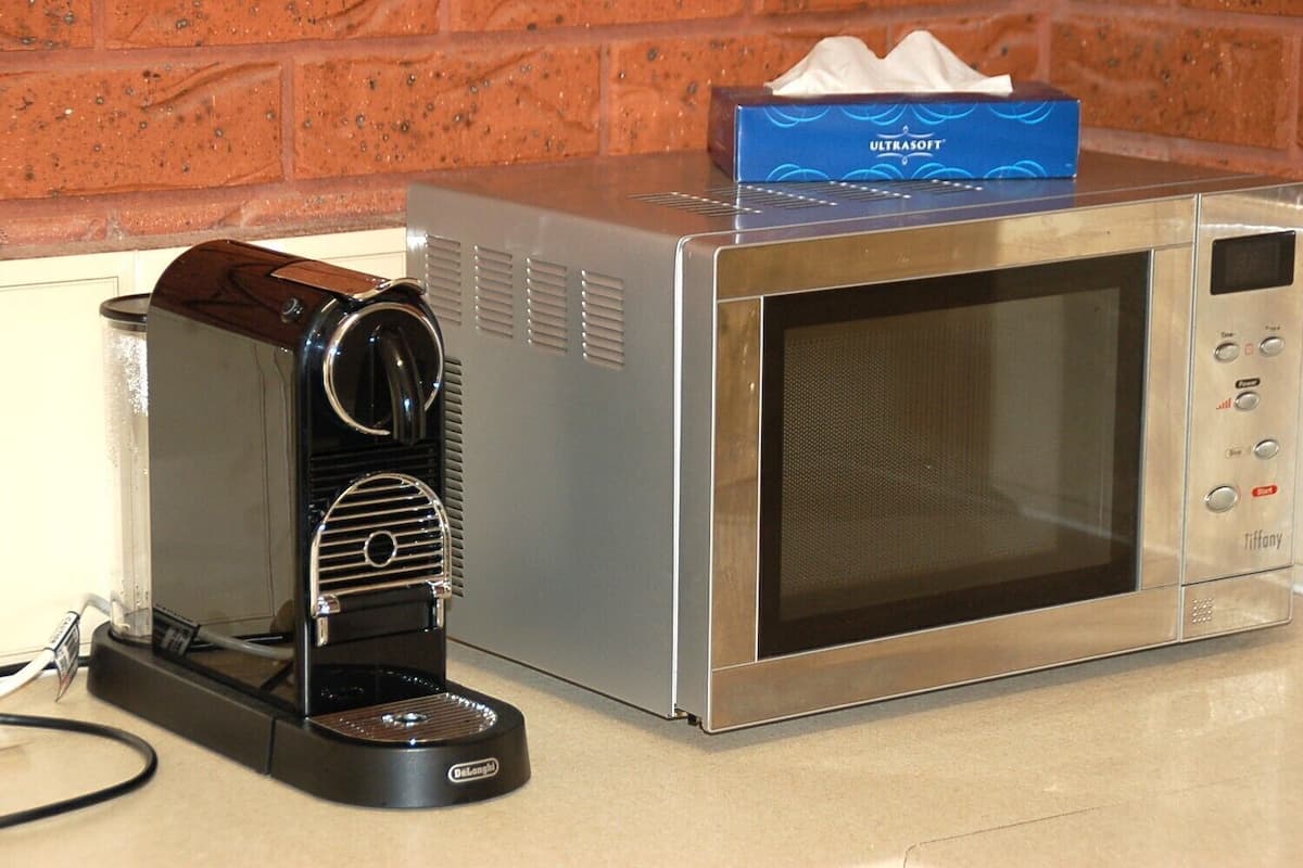 A microwave oven with a coffee maker and a tissue box on top.