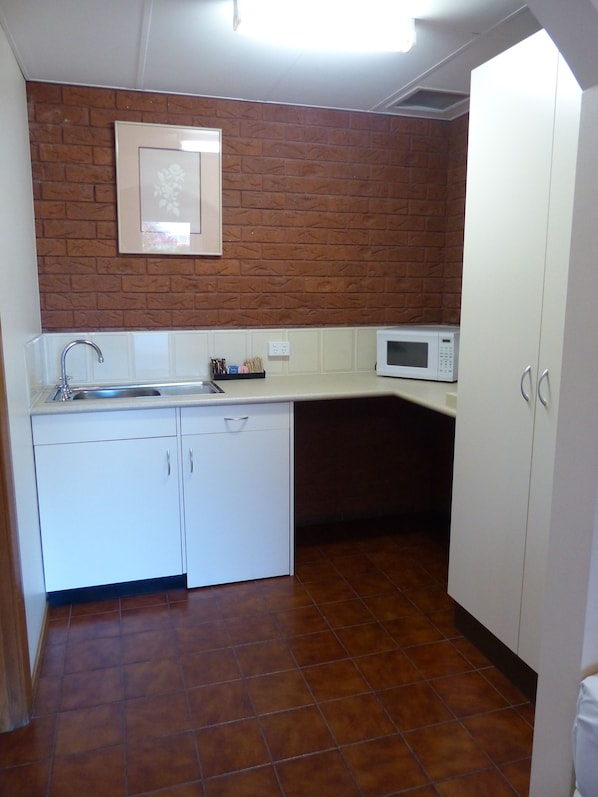 A compact kitchen with a sink, a microwave, and white cabinets.