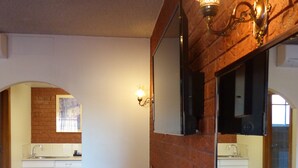 A hotel room with a large bed, a bedside telephone, a mirror, and a brick wall. - Meramie Motor Inn (Albury)
