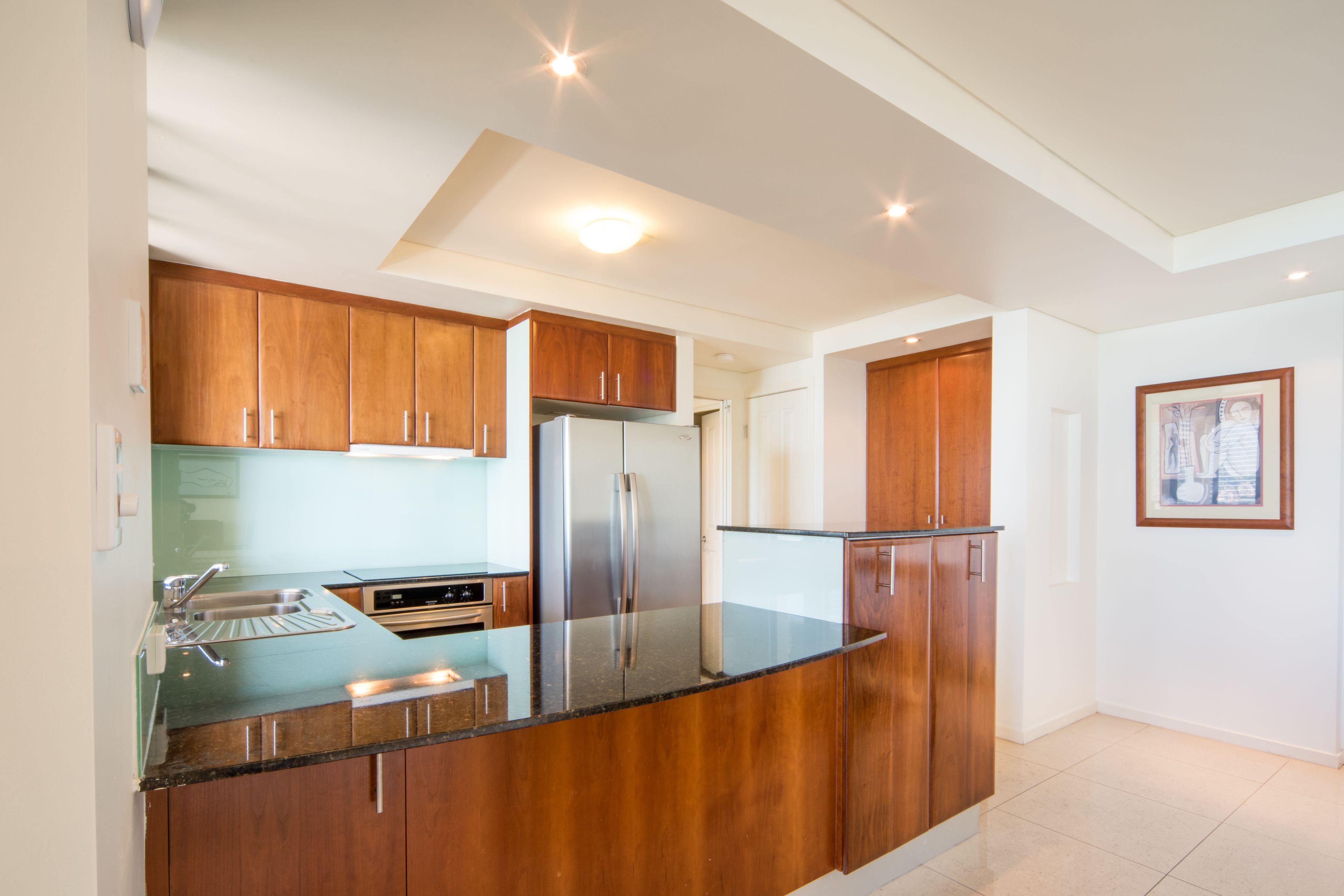 A modern kitchen with wooden cabinets, stainless steel appliances, and a glass countertop.