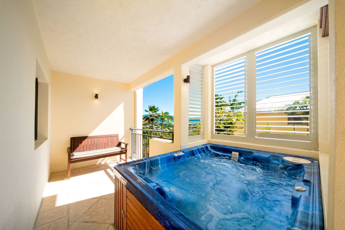Zona de spa con hidromasaje, una banca y vista a palmeras a través de la ventana.