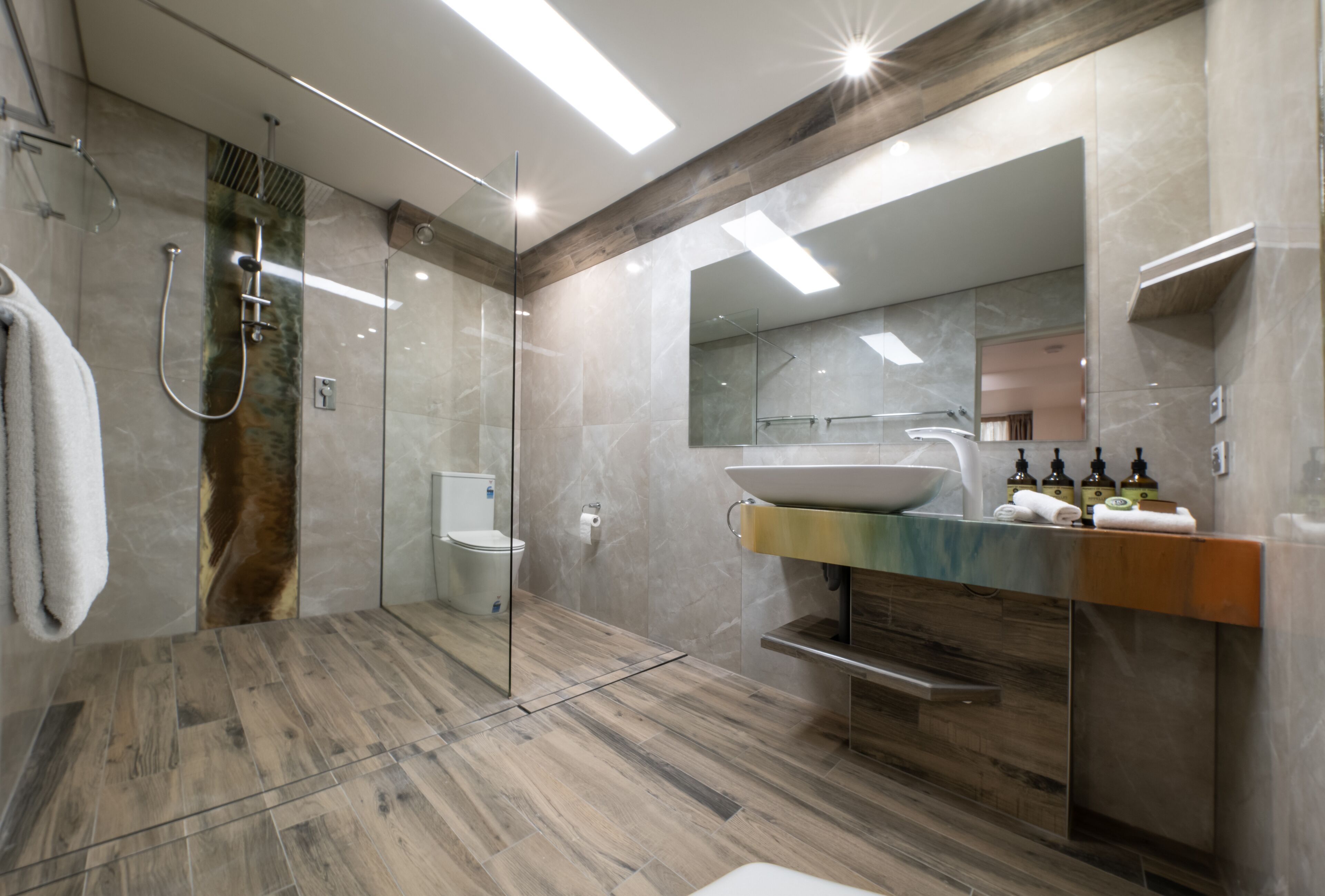 Ein modernes Badezimmer mit einer gläsernen Duschkabine, einem großzügigen Waschbecken mit Marmorplatte und Holzboden.