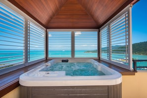 Un jacuzzi con techo de madera y grandes ventanales con vista al mar turquesa.