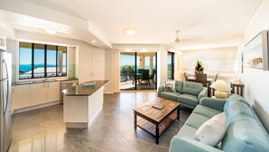 A modern kitchen with a view, a dining area with a table and chairs, and a living room with a sofa and a coffee table. - Pinnacles (Airlie Beach)