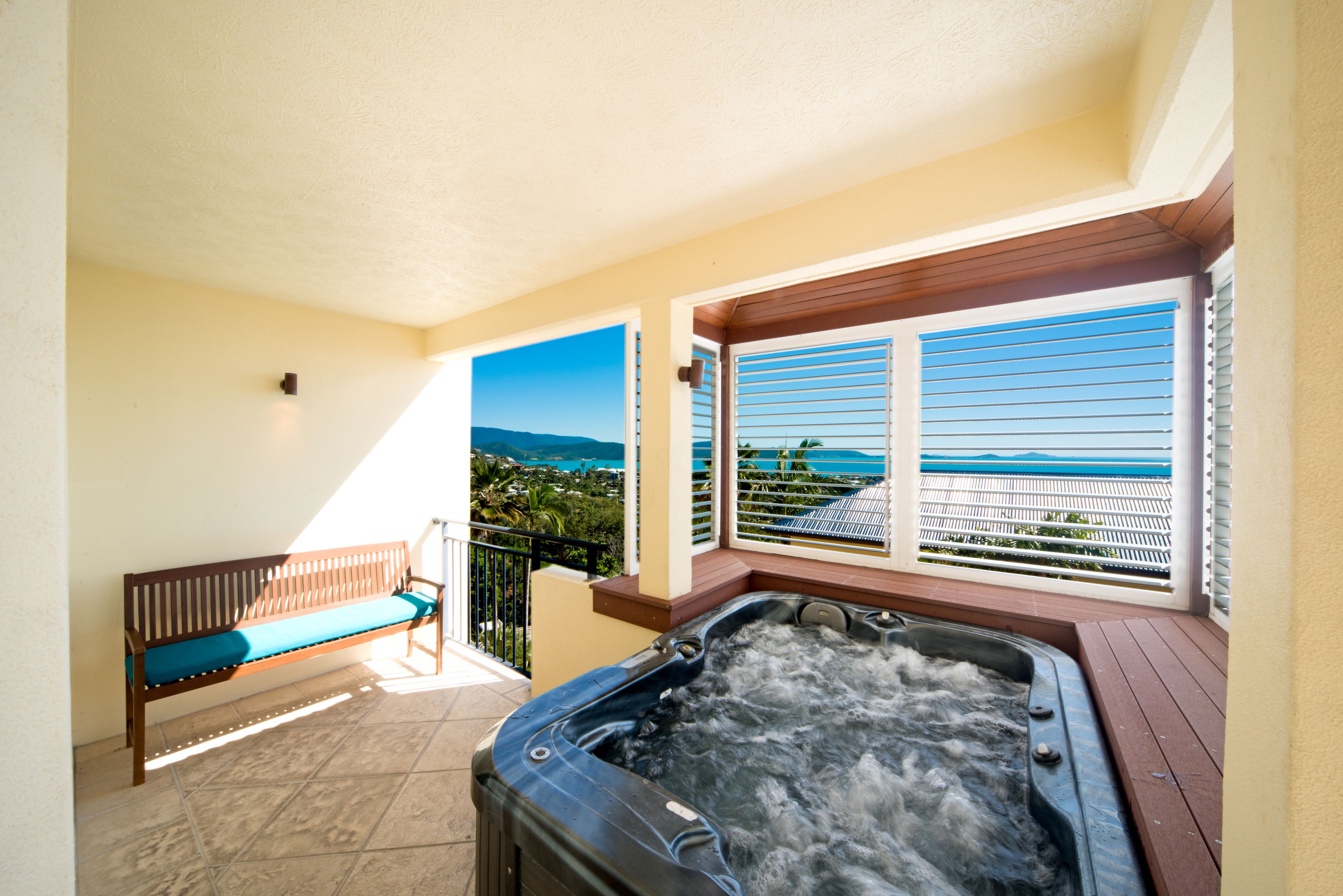 A balcony with a hot tub, a wooden bench, and a view of the ocean.