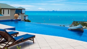 A swimming pool with lounge chairs and a view of the ocean. - Pinnacles (Airlie Beach)