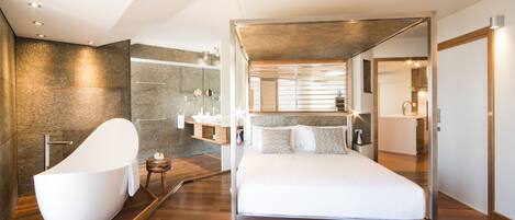 Un dormitorio moderno con una cama grande, una bañera independiente y una ducha a pie.